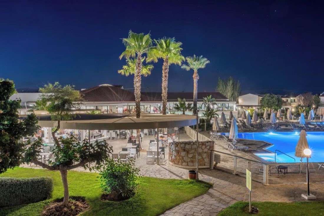 The resort by night, lit pool, palm trees and the pool bar